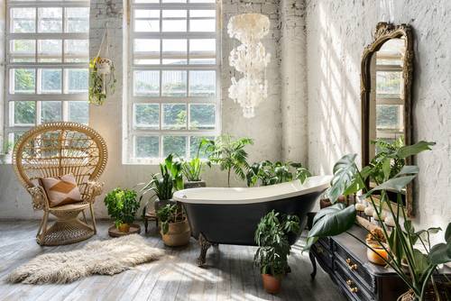 Bohemski slog kopalnice, kjer kraljujejo rastline, lestenec, preproga, stol in ogromno ogledalo.