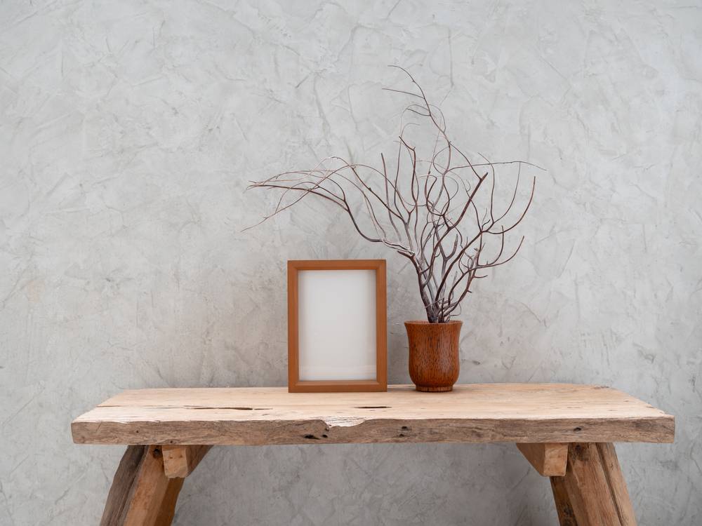 Masivna lesena miza z vazo in okvirjem za sliko, v ozadju betonska stena.