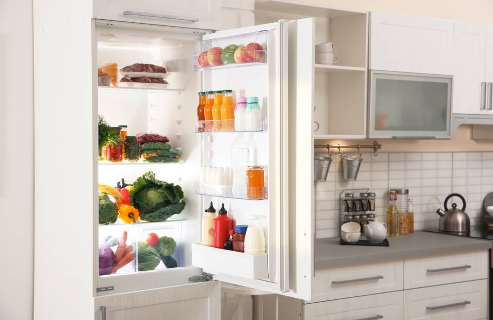 Pogled na poln hladilnik zelenjave in drugih živil, ki se stilsko sklada z ostalimi kuhinjskimi elementi.