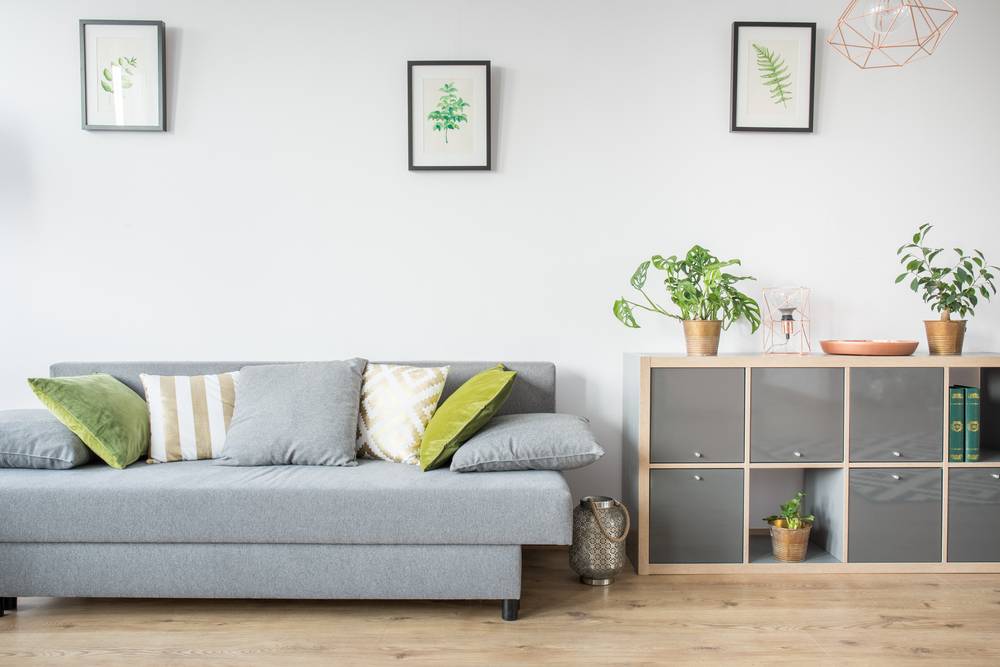 Moderna dnevna soba nevtralnih barv, opremljena s kavčem, pisanimi blazinami in omarico.