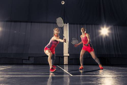 Dve dekleti med igro badmintona v dvojicah, ki je odlična rekreacija za krepitev celega telesa.