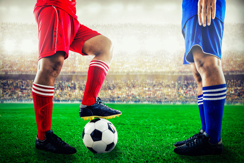 Pogled na poln stadion, nogometno žogo in dvoboj med modro in rdečo nogometno ekipo.