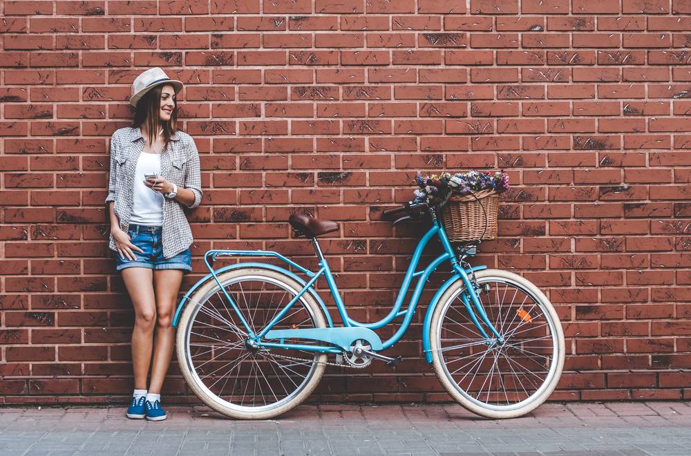 Nasmejana ženska stoji zraven »vintage« mestnega kolesa s košaro, polno cvetlic.