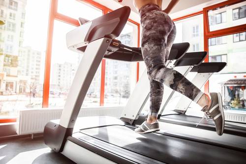 Ženska teče na fitnes tekalni stezi, s katero lahko nadomestite tek v naravi.