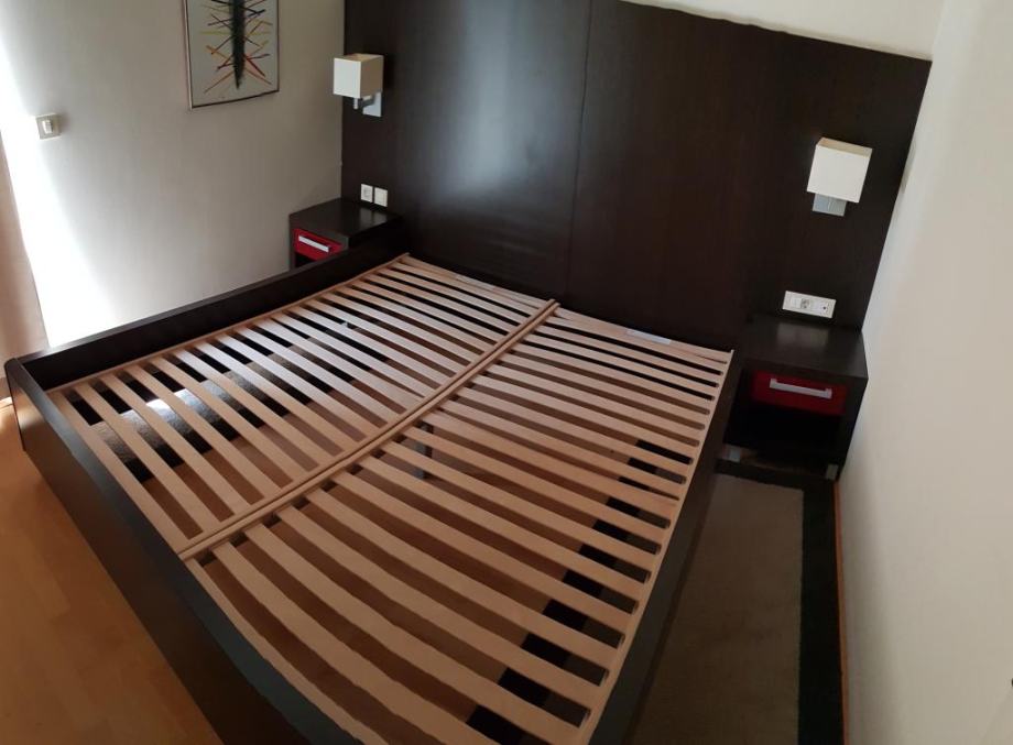 Postelja z dvema nočnima omaricama in leseno steno